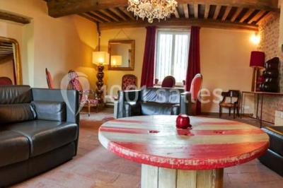 Salon rustique avec poutres apparentes, cheminée, mobilier en cuir et table basse en bois rouge dans un cadre chaleureux.