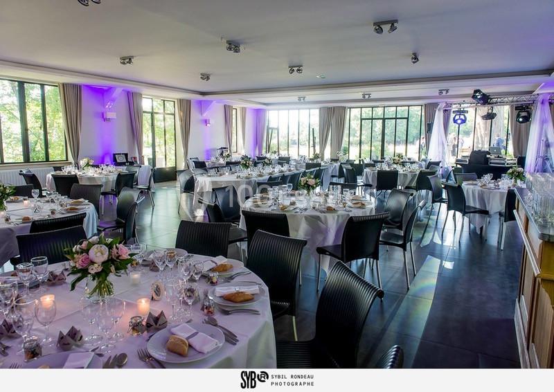Salle de réception élégamment décorée avec des tables rondes dressées pour un événement, éclairée par la lumière naturelle.