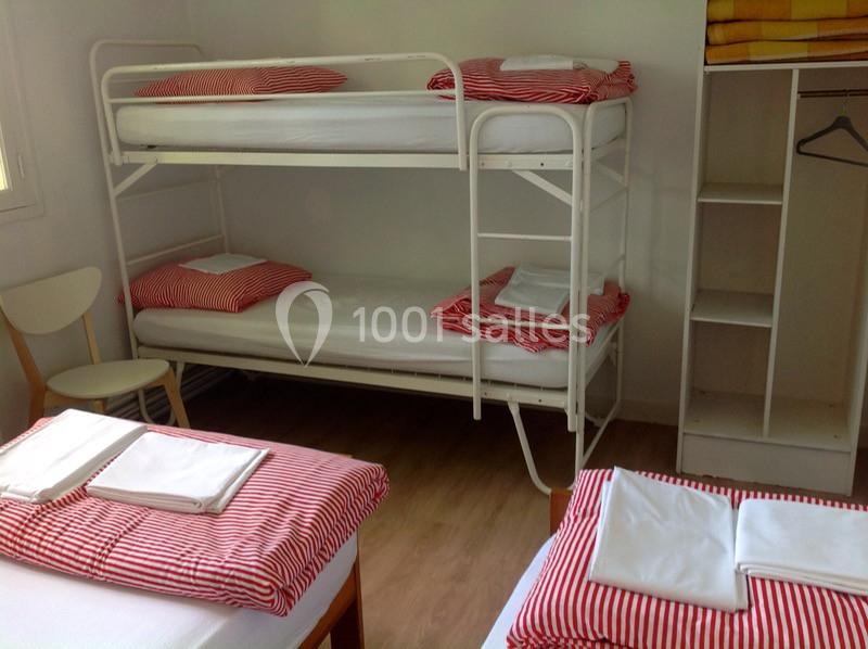 Chambre avec lits superposés et lit simple, draps à rayures rouges, étagère ouverte et chaise en bois.