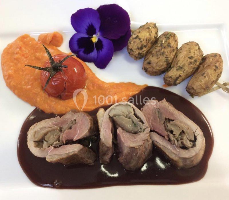 Assiette gastronomique avec viande roulée, sauce brune, purée orange, tomates cerises, pommes de terre et fleur comestible.