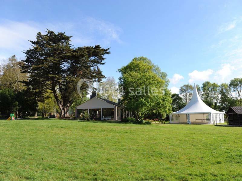 Grand espace vert avec une pelouse, un grand arbre, une structure en toile blanche et un bâtiment en arrière-plan.