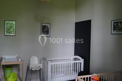 Une chambre d'enfant avec un lit bébé, une table à langer, une chaise haute et des cadres accrochés au mur.