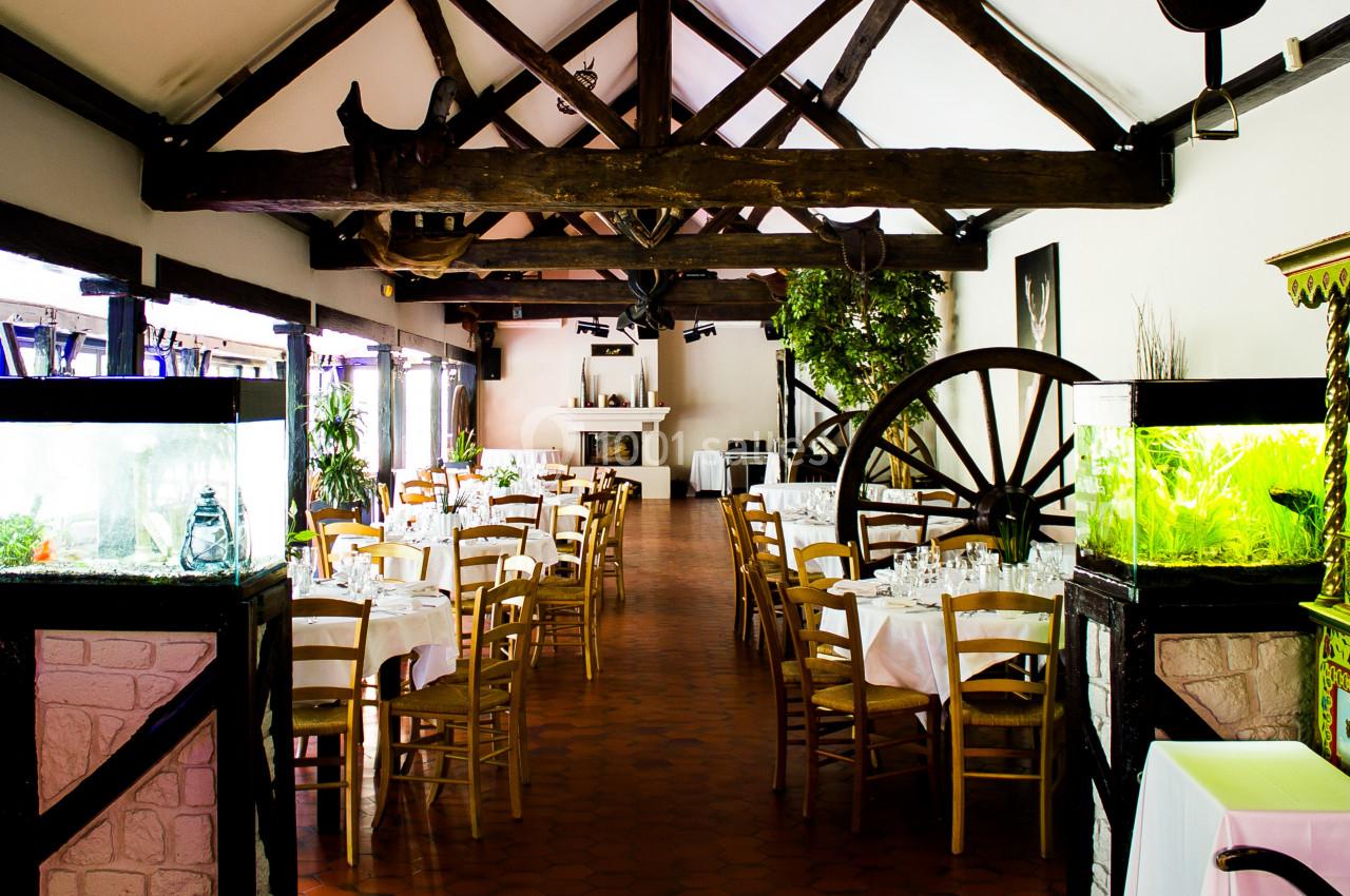 Salle de restaurant lumineuse avec poutres apparentes, tables dressées et aquariums décoratifs.