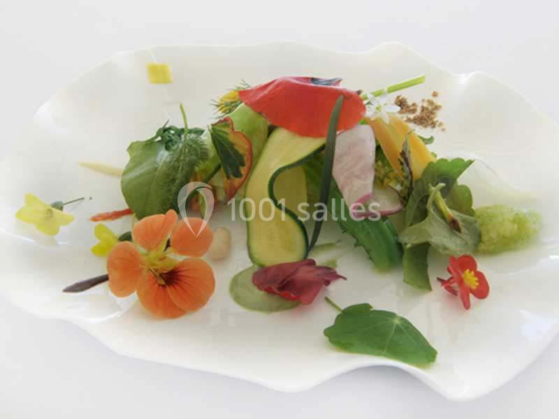 Assiette garnie de légumes frais, fleurs comestibles et herbes, présentée de manière artistique sur un fond blanc.