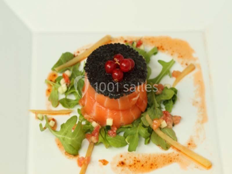 Entrée composée de saumon fumé, caviar, groseilles, roquette et sauce, présentée sur une assiette blanche.