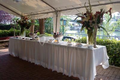 Salle lumineuse avec une grande table rectangulaire dressée, entourée de chaises décorées, parquet clair et fenêtres donnant…