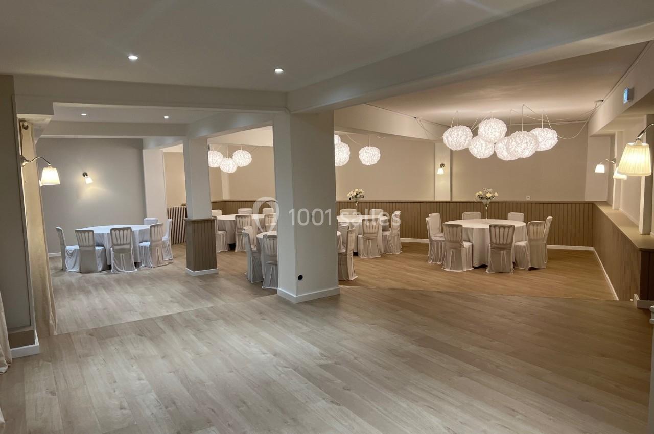 Salle de réception lumineuse avec tables rondes dressées, chaises blanches et suspensions décoratives modernes.