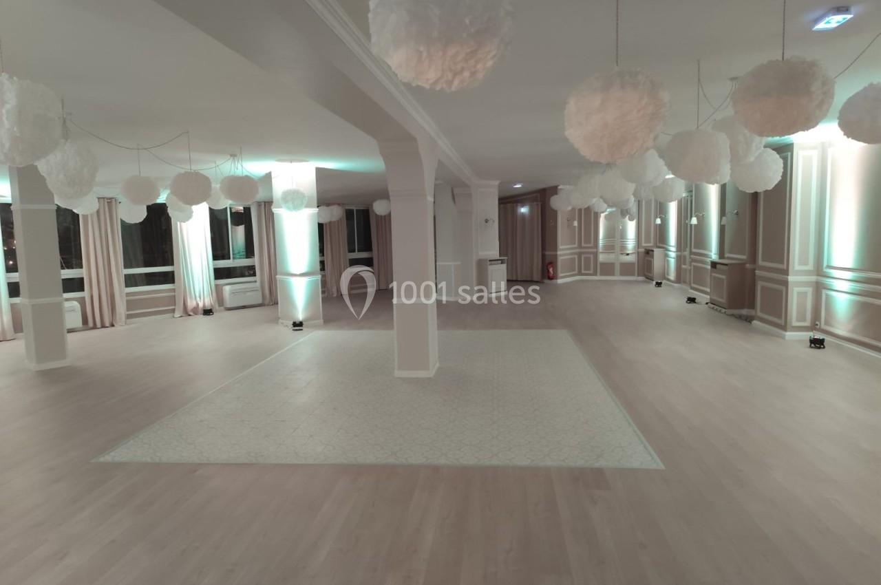 Salle spacieuse avec parquet clair, colonnes blanches et suspensions décoratives en forme de nuages.