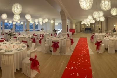 Salle lumineuse avec une grande table rectangulaire dressée, entourée de chaises décorées, parquet clair et fenêtres donnant…