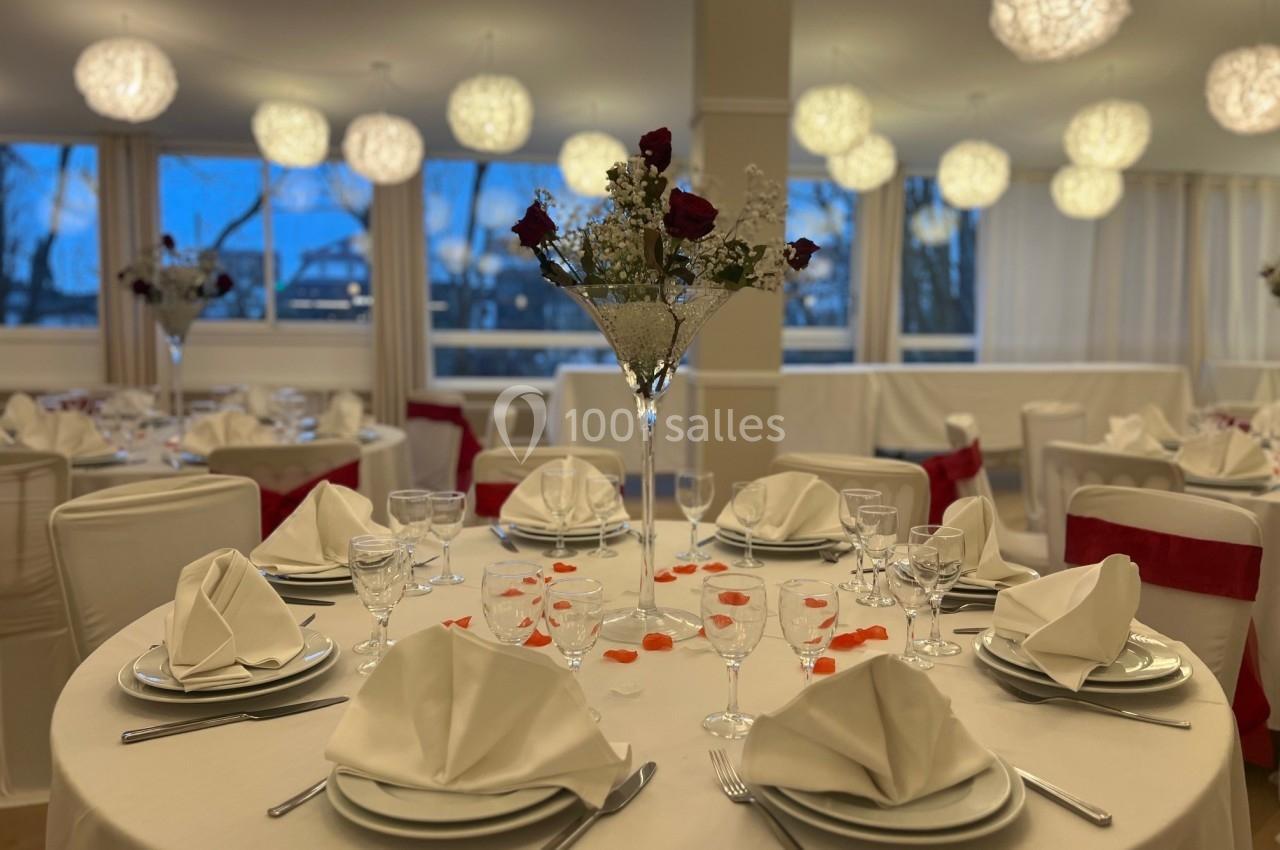 Salle de réception décorée avec des tables rondes dressées, nappes blanches et centre de table floral.
