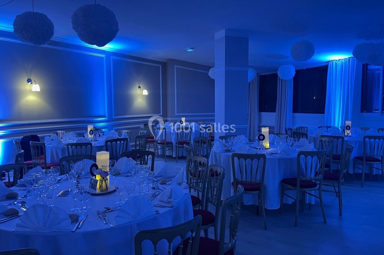 Salle de réception décorée avec des tables rondes dressées, éclairée par une lumière bleue tamisée.