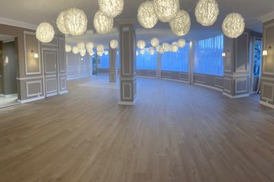 Salle lumineuse avec une grande table rectangulaire dressée, entourée de chaises décorées, parquet clair et fenêtres donnant…