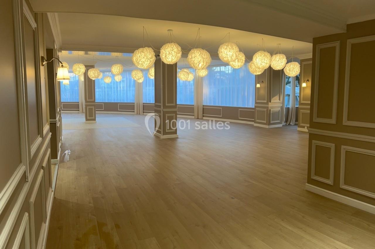 Salle spacieuse avec parquet clair, murs ornés de moulures et suspensions lumineuses en forme de sphères.