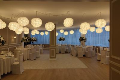 Salle lumineuse avec une grande table rectangulaire dressée, entourée de chaises décorées, parquet clair et fenêtres donnant…