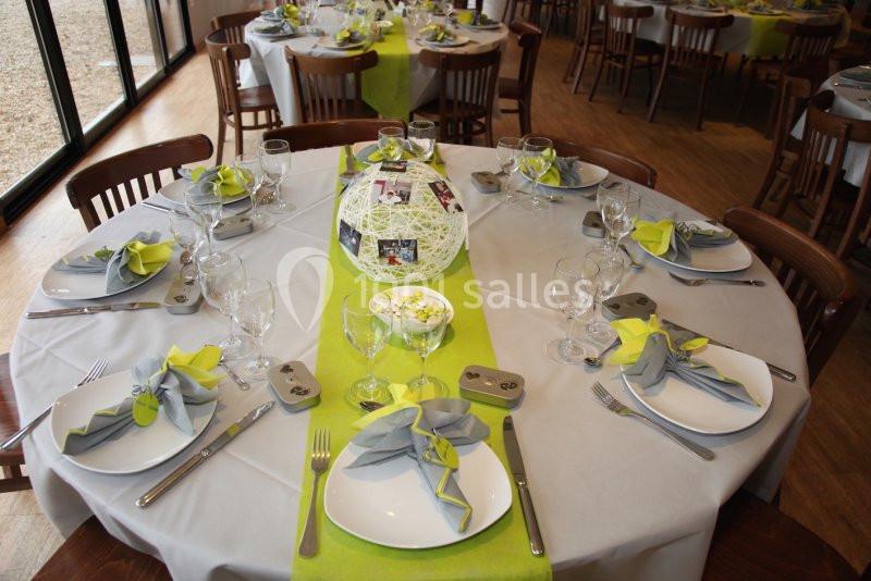 Tables rondes dressées avec nappes grises, chemins de table verts, serviettes pliées et centre de table décoratif.