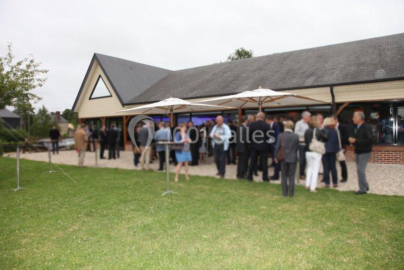 Groupe de personnes rassemblées à l'extérieur d'un bâtiment, discutant sous des parasols sur une pelouse.