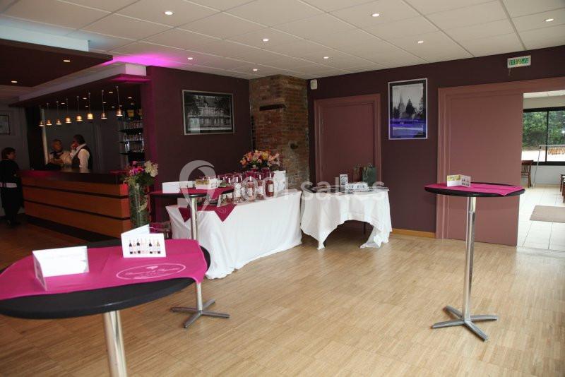Salle avec un bar, des tables hautes et des présentoirs décorés de nappes roses, dans un cadre lumineux.