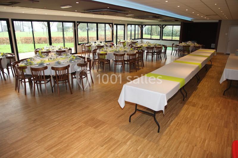Salle de réception lumineuse avec tables dressées et nappes blanches, entourée de grandes baies vitrées donnant sur un…