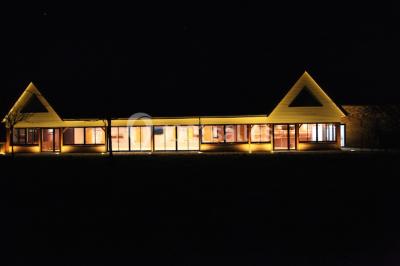 Bâtiment illuminé de nuit avec des façades vitrées et un toit en pente, entouré d'obscurité.