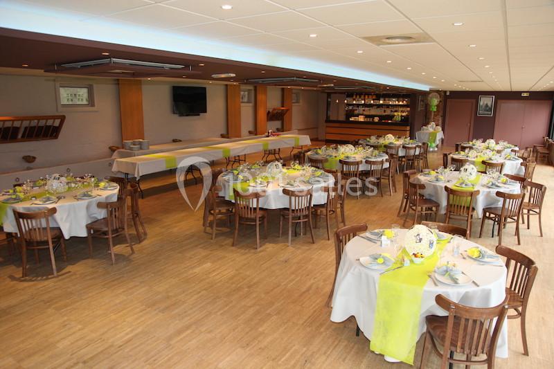 Salle de réception aménagée avec des tables rondes décorées de nappes blanches et vertes, prête pour un événement.