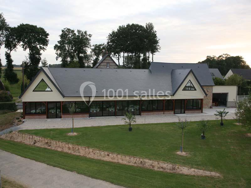 Bâtiment moderne avec façade vitrée, entouré de pelouse et d'arbres, sous un ciel légèrement nuageux.