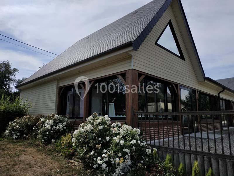 Maison avec façade en bois clair, grandes fenêtres triangulaires et jardin fleuri à l'avant.