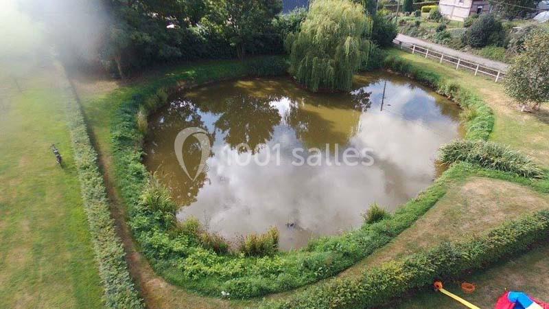 Vue aérienne d'un petit étang entouré de verdure, avec des arbres et des reflets de nuages à la surface de l'eau.
