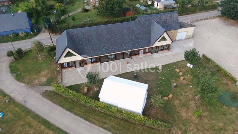 Vue aérienne d'un bâtiment avec toit en ardoise, entouré de verdure, d'une route et d'une structure blanche temporaire.