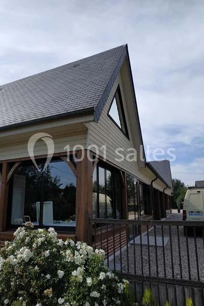 Maison à toit en pente avec de grandes fenêtres, entourée de fleurs blanches et d'une allée gravillonnée.