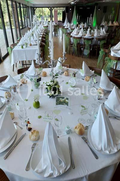 Salle de réception décorée avec des tables rondes et rectangulaires, nappes blanches, serviettes pliées et centres de table…
