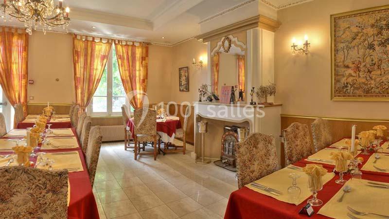 Salle de restaurant élégante avec nappes rouges, chaises décorées, cheminée ornée et lumière naturelle.