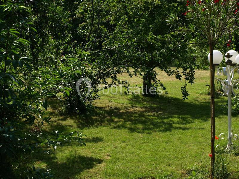 Un jardin verdoyant avec des arbres, un lampadaire blanc et des arbustes sous une lumière naturelle.