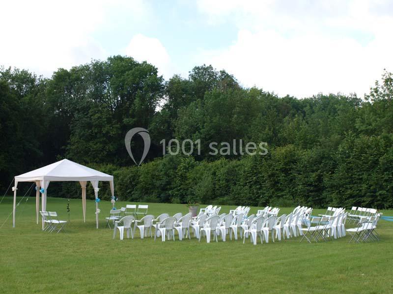 Chaises blanches disposées en extérieur sous une tente et sur une pelouse, entourées d'arbres.