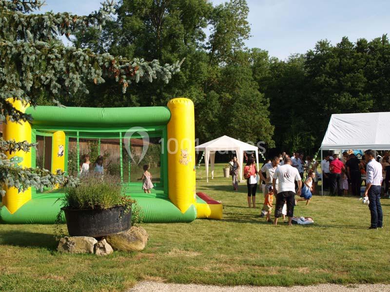 Structure gonflable verte et jaune avec des enfants jouant, entourée d'adultes et de tentes dans un espace extérieur.