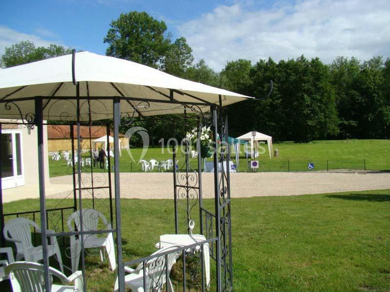 Tonnelle en fer forgé avec chaises blanches, donnant sur une pelouse et des arbres en arrière-plan.