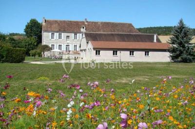 Arche de cérémonie décorée de fleurs blanches et de voilages verts, installée dans un jardin ombragé.