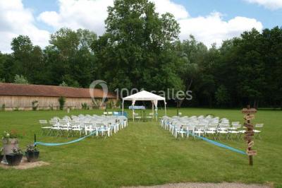 Arche de cérémonie décorée de fleurs blanches et de voilages verts, installée dans un jardin ombragé.