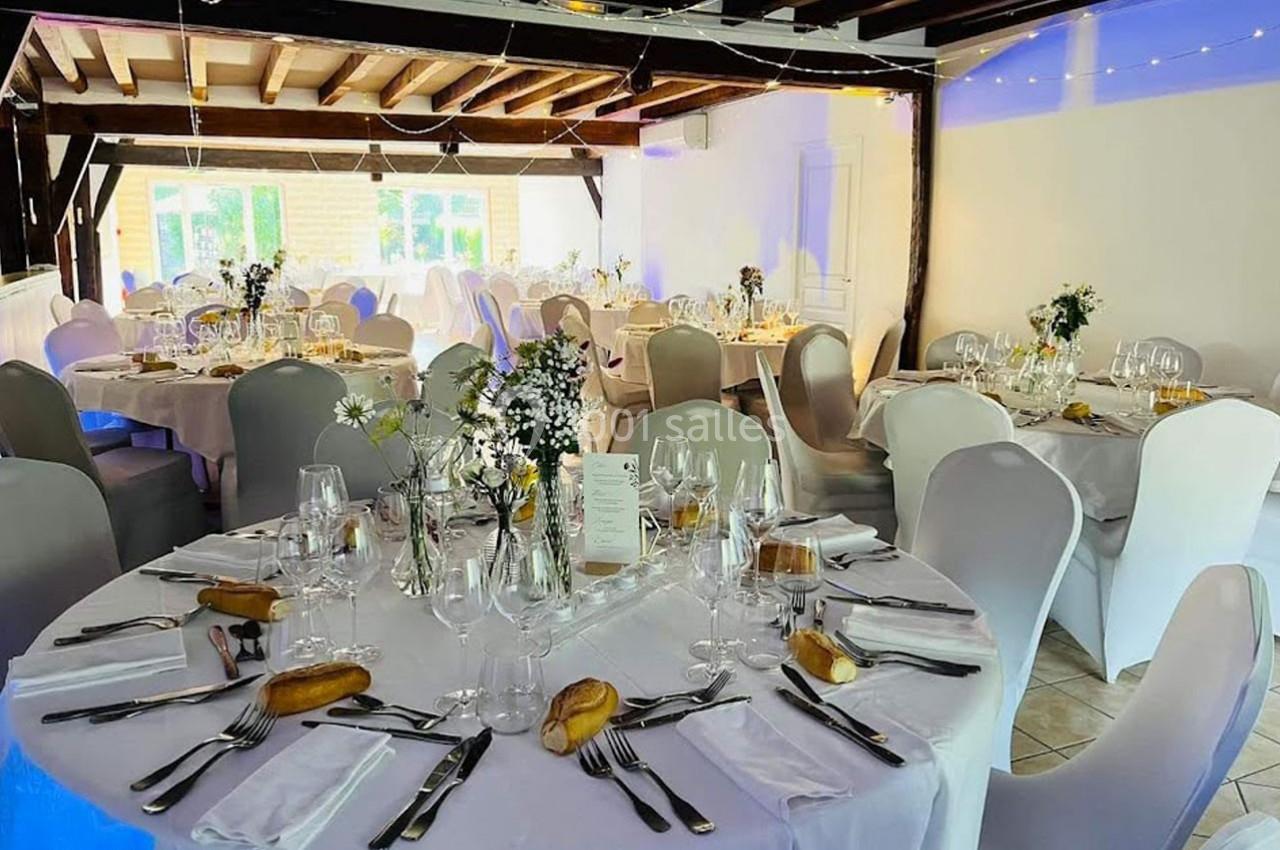 Salle de réception décorée avec des tables rondes dressées, nappes blanches, vaisselle élégante et éclairage chaleureux.