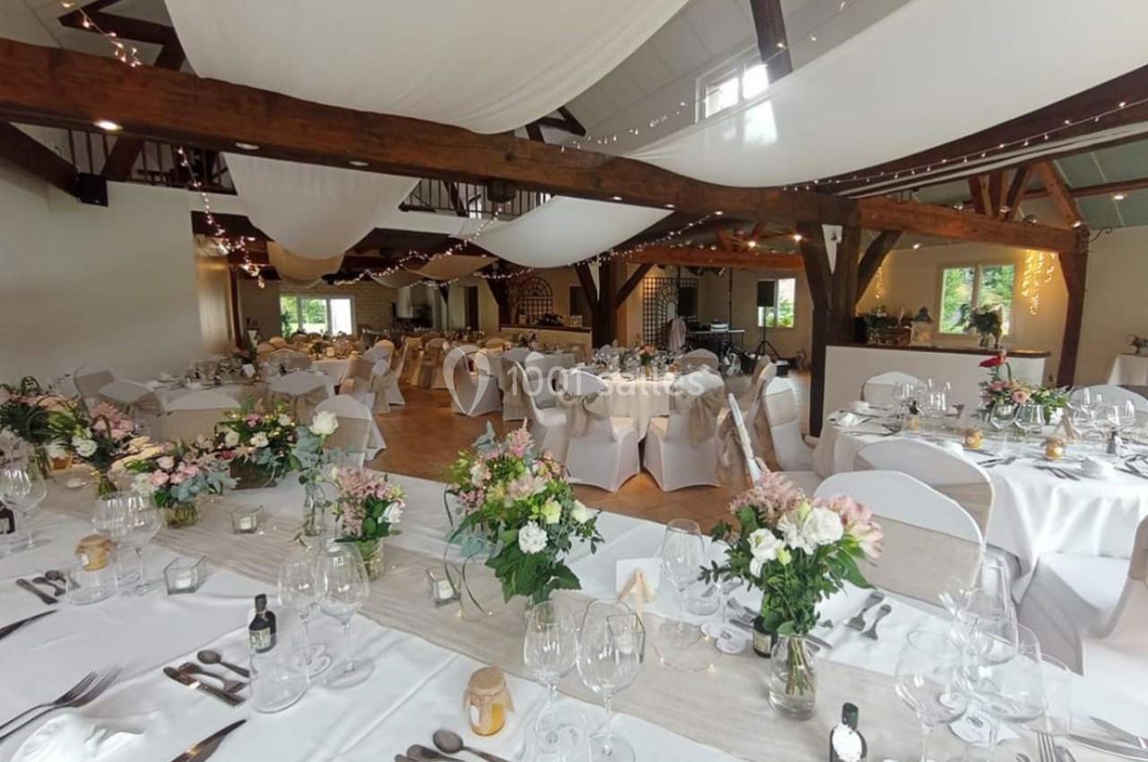 Salle de réception décorée pour un mariage, avec tables dressées, fleurs, nappes blanches et guirlandes lumineuses…