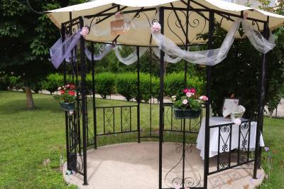 Arche de cérémonie décorée de fleurs blanches et de voilages verts, installée dans un jardin ombragé.