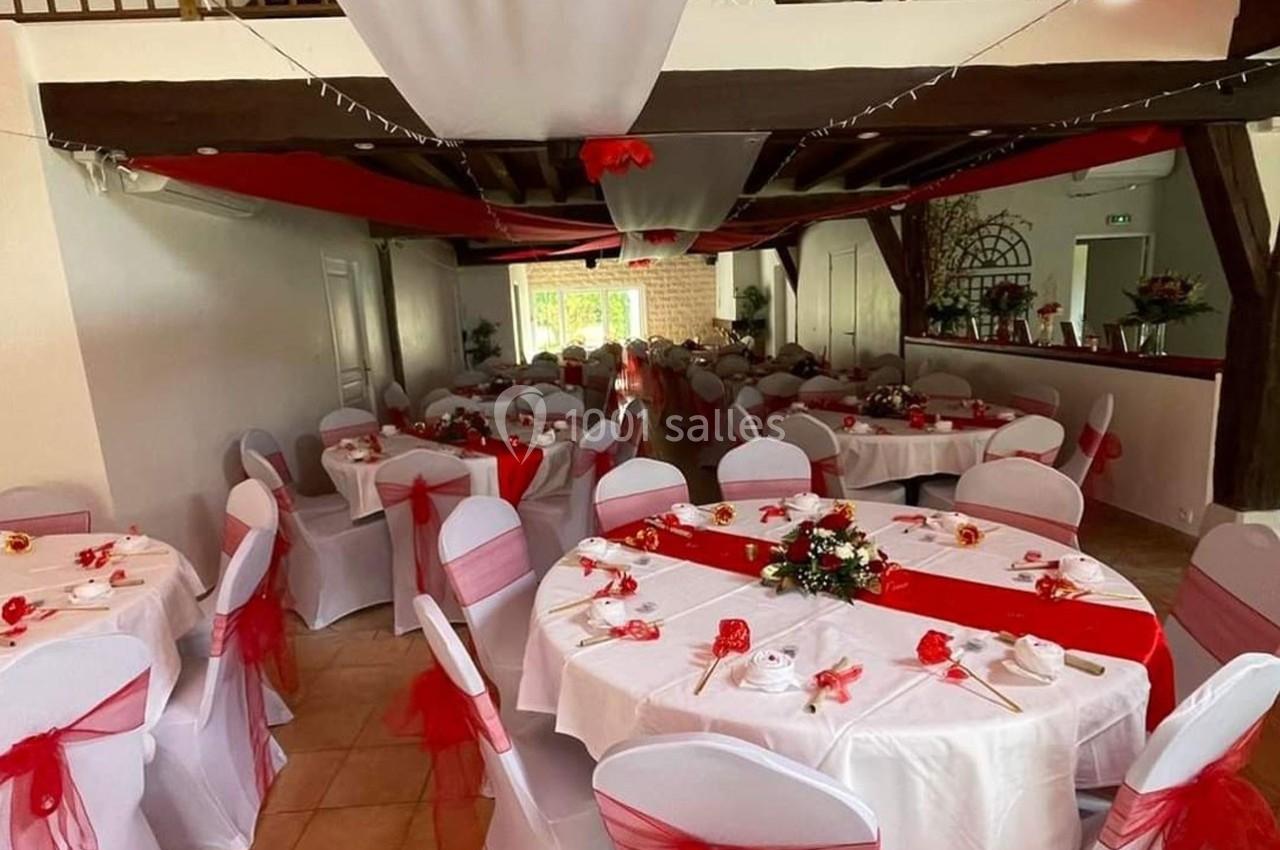 Salle de réception décorée avec des nappes blanches, des chaises ornées de nœuds rouges et des tables fleuries.