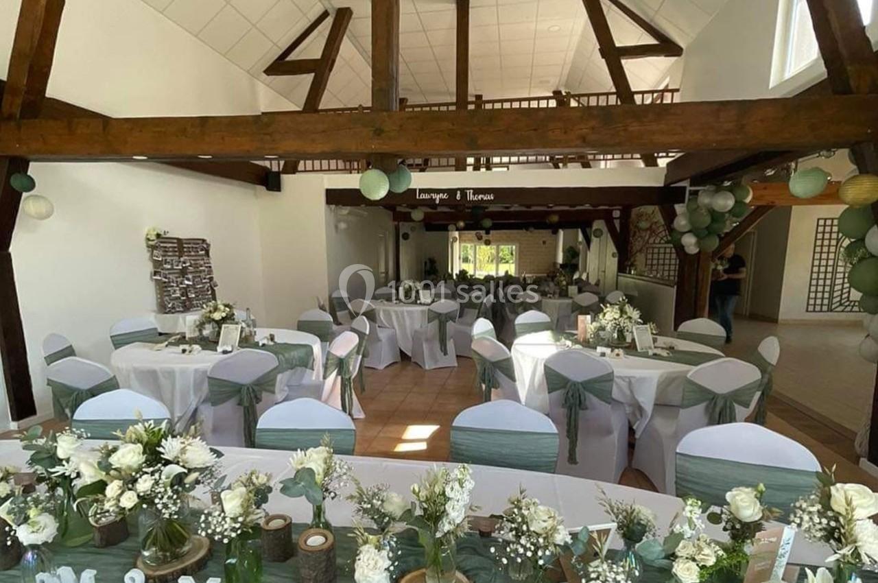 Salle de réception décorée pour un mariage, avec tables rondes ornées de nappes blanches et de centres de table floraux.