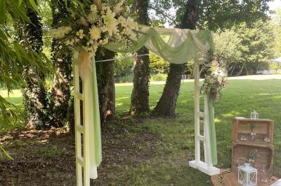 Arche de cérémonie décorée de fleurs blanches et de voilages verts, installée dans un jardin ombragé.
