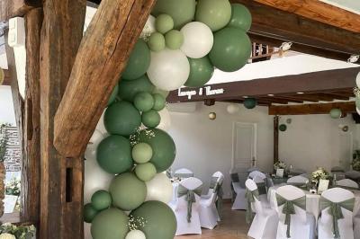 Arche de cérémonie décorée de fleurs blanches et de voilages verts, installée dans un jardin ombragé.