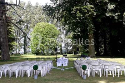 Terrasse en bois longeant un bâtiment en briques avec vue sur un jardin arboré sous un ciel bleu.