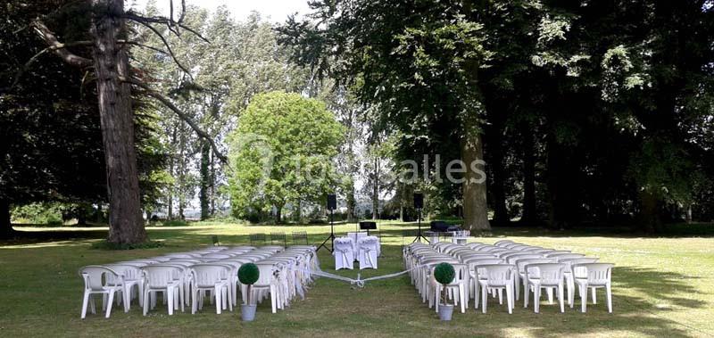 Chaises blanches disposées en rangées sur une pelouse, face à une table décorée, dans un cadre arboré.