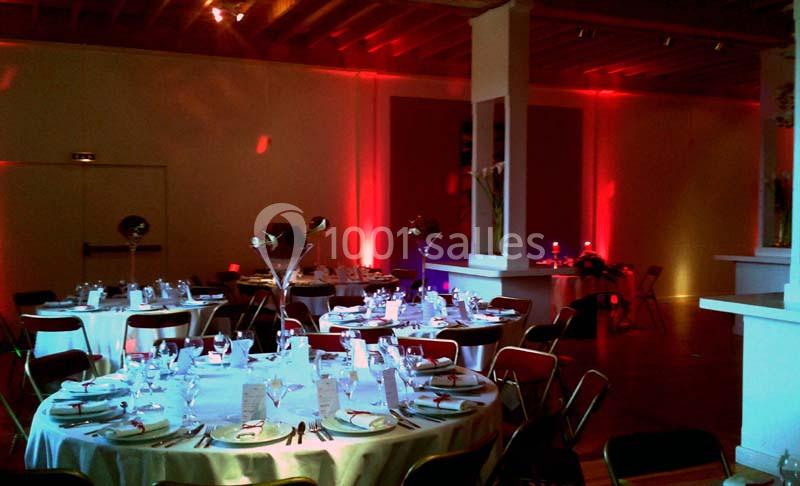 Salle de réception décorée avec des tables rondes dressées, éclairage tamisé et ambiance chaleureuse.