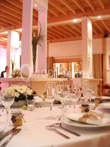 Table dressée avec vaisselle élégante, fleurs blanches et décoration raffinée dans une salle lumineuse au plafond en bois.