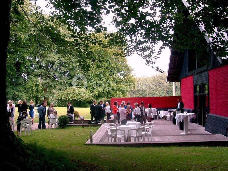 Groupe de personnes rassemblées sur une terrasse en bois près d'un bâtiment rouge, entourées de verdure.