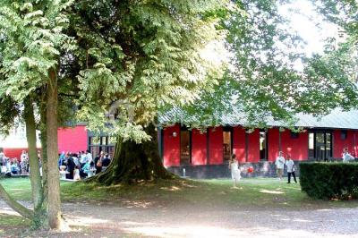 Terrasse en bois longeant un bâtiment en briques avec vue sur un jardin arboré sous un ciel bleu.